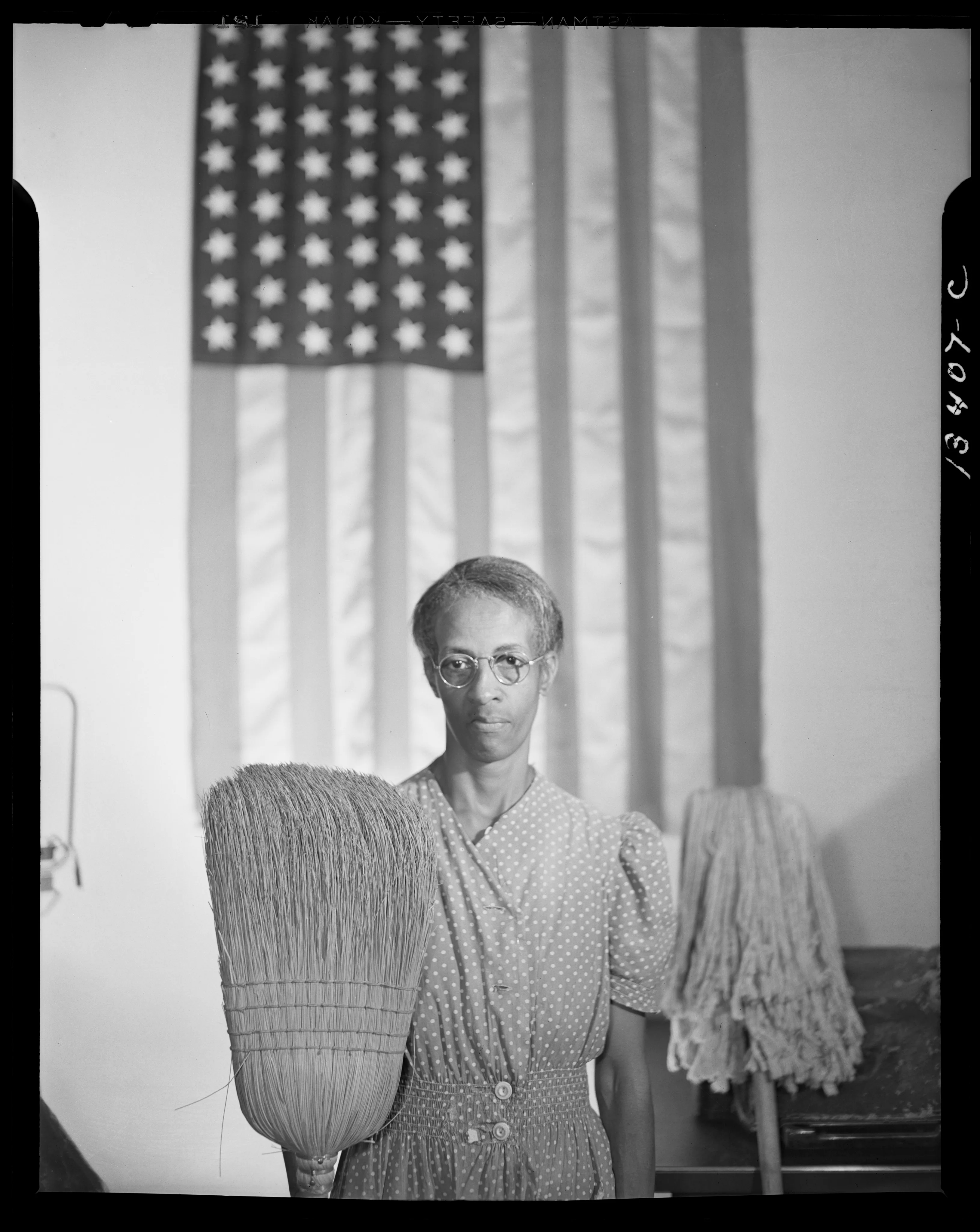 A cleaner holds a broom and mop before a hanging United States flag.